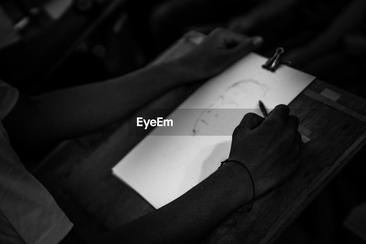 Cropped image of person sketching on paper in darkroom