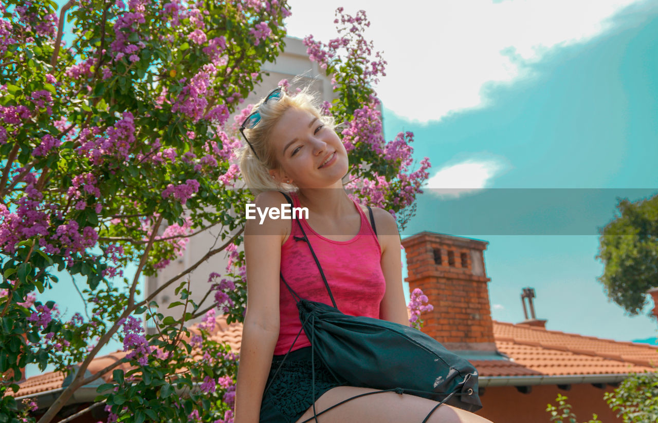 Low angle portrait of woman against pink flowering plants