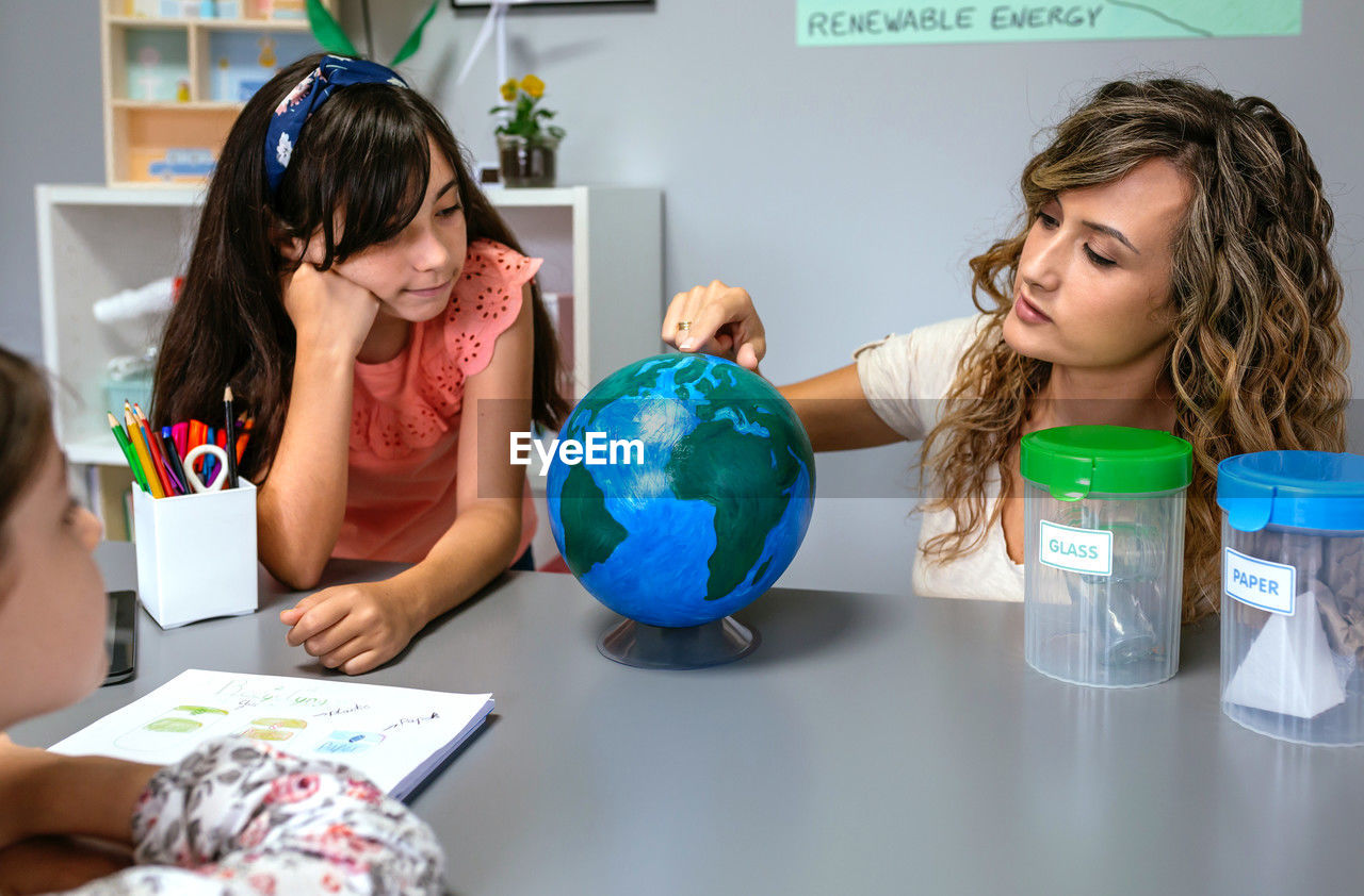 Female teacher giving ecology lesson with handmade globe world to girl students