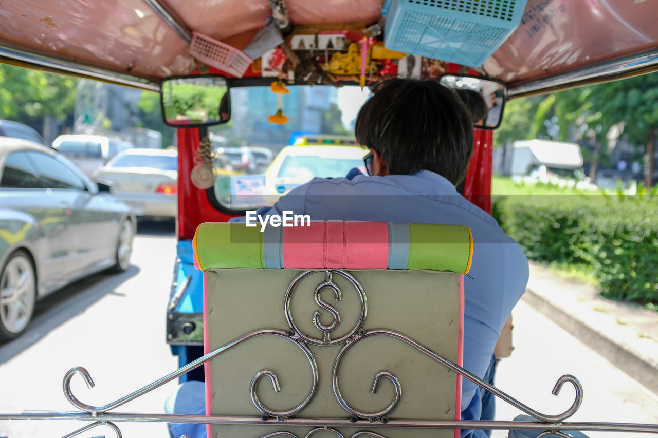 REAR VIEW OF MAN SITTING ON CAR IN CITY