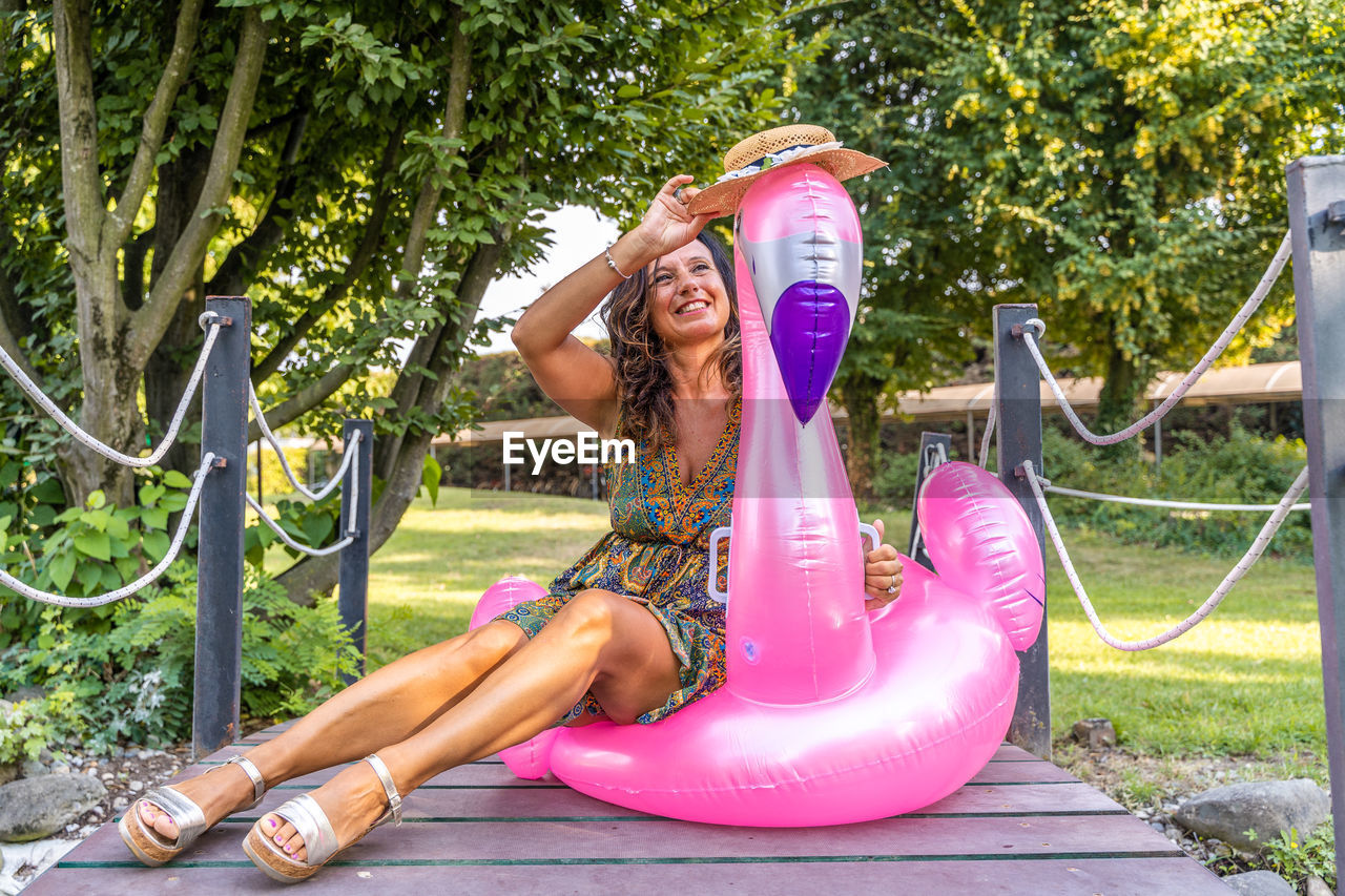 Portrait of beautiful middle aged woman sitting on pink flamingo inflatable toy