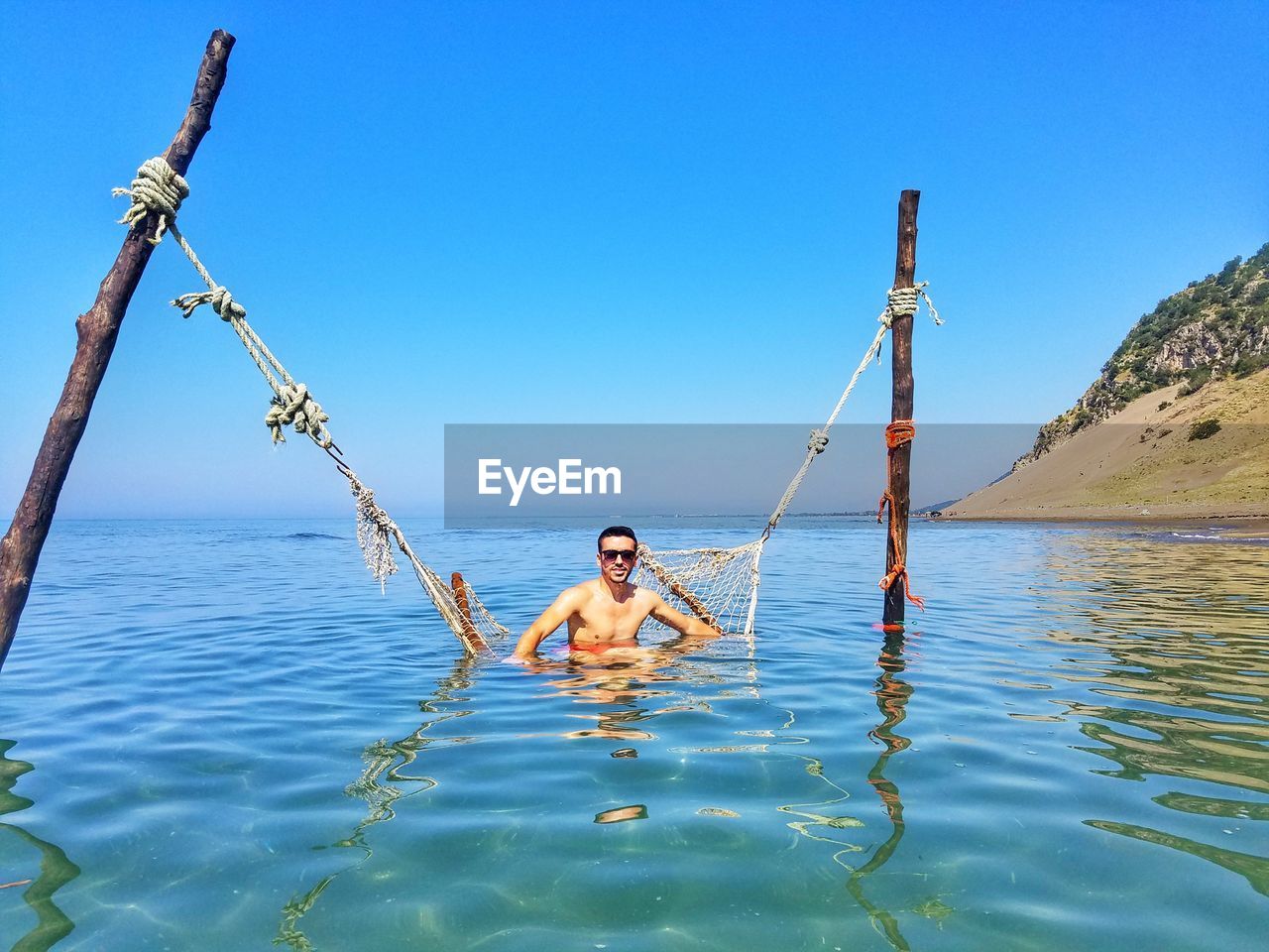 Full length of shirtless man in sea against clear blue sky