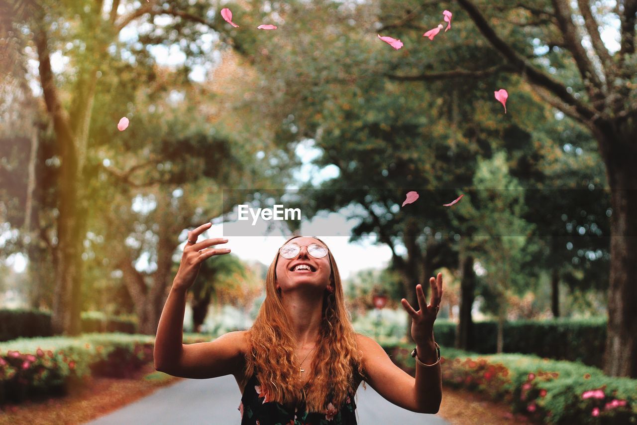 Young woman throwing petal mid-air while standing at park