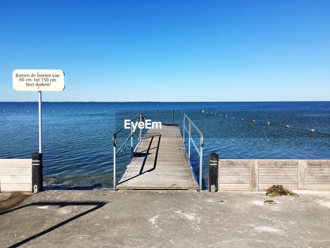 Pier leading towards sea against clear sky during sunny day