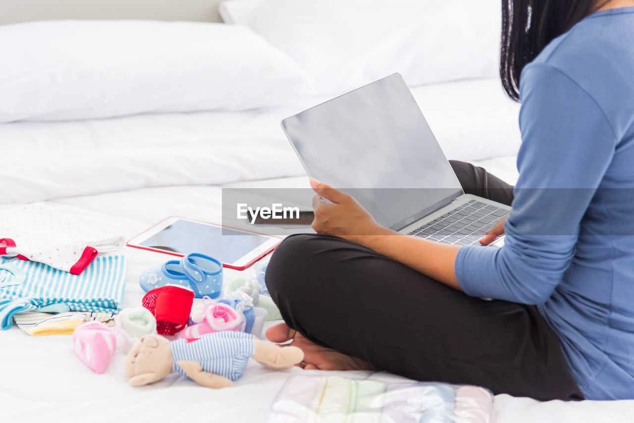 Low section of woman using laptop while sitting on bed at home