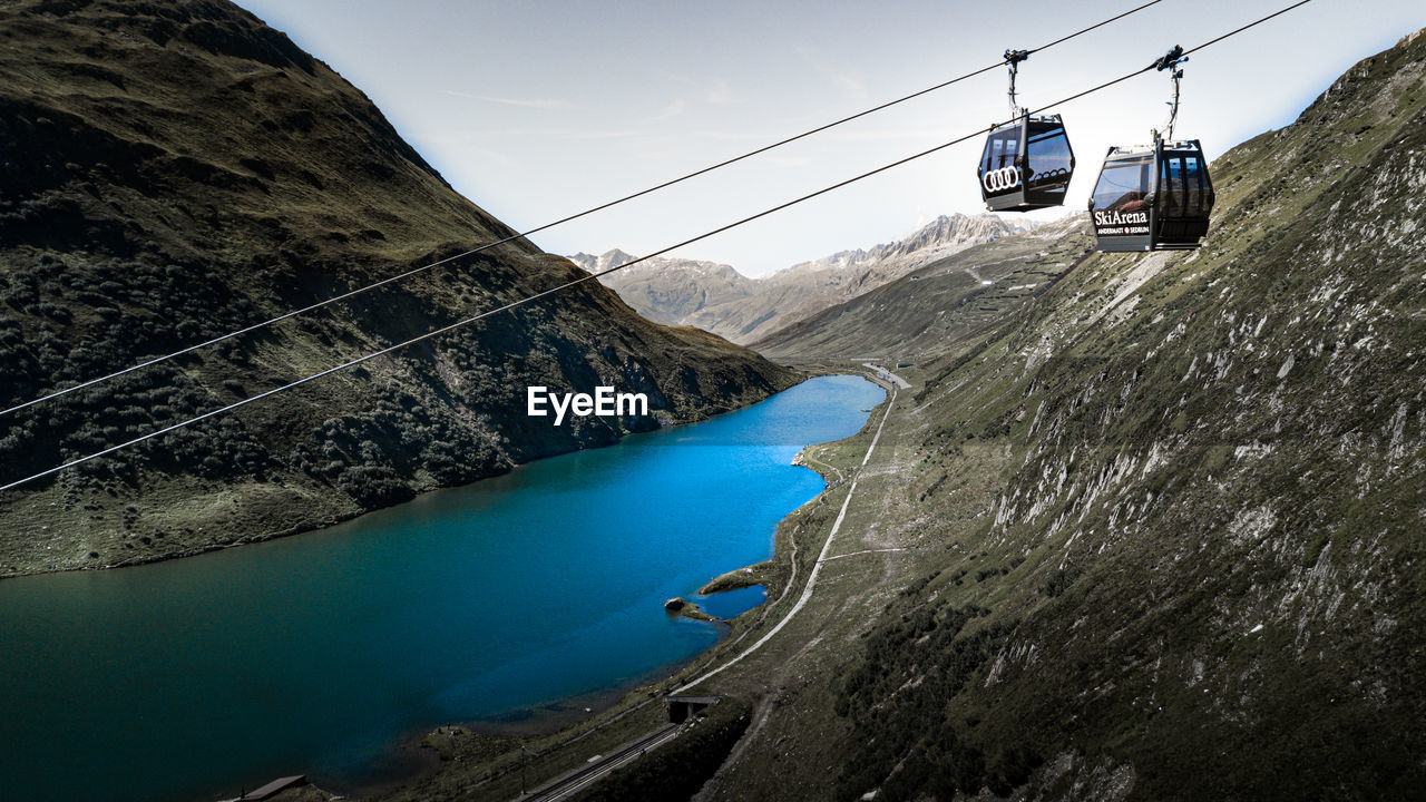 HIGH ANGLE VIEW OF OVERHEAD CABLE CAR OVER SEA AGAINST MOUNTAINS
