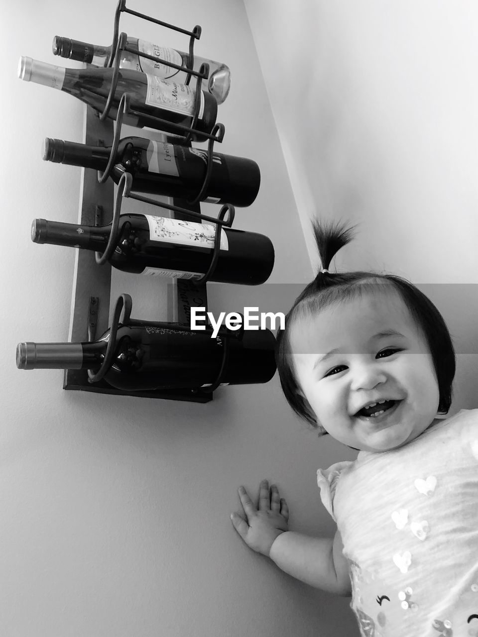 Portrait of smiling girl standing by wine bottles in rack on wall