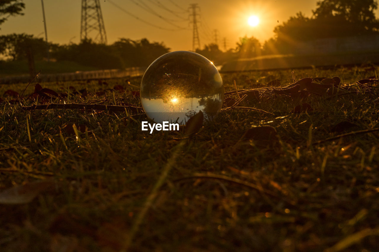 Close-up of crystal ball on field against sky during sunset