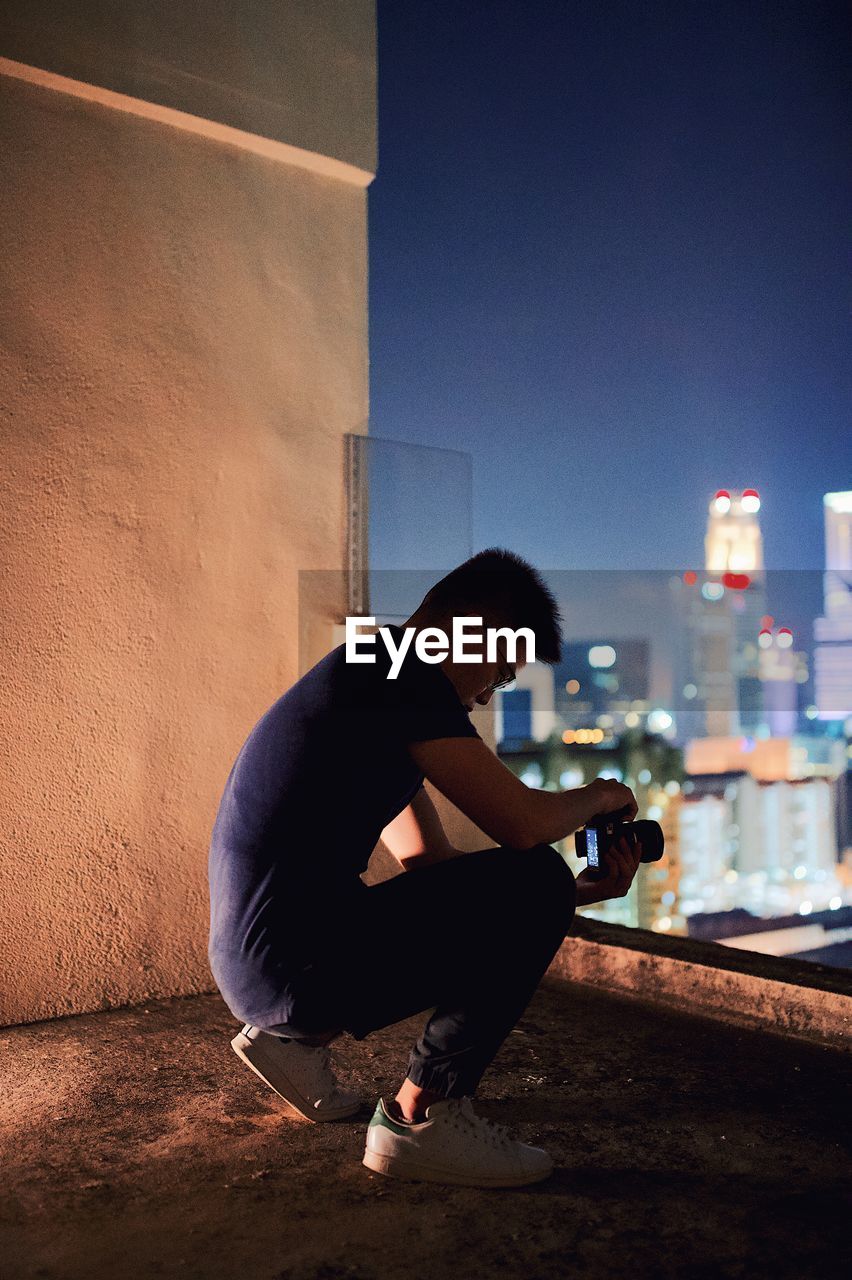 Young man crouching on building terrace at night