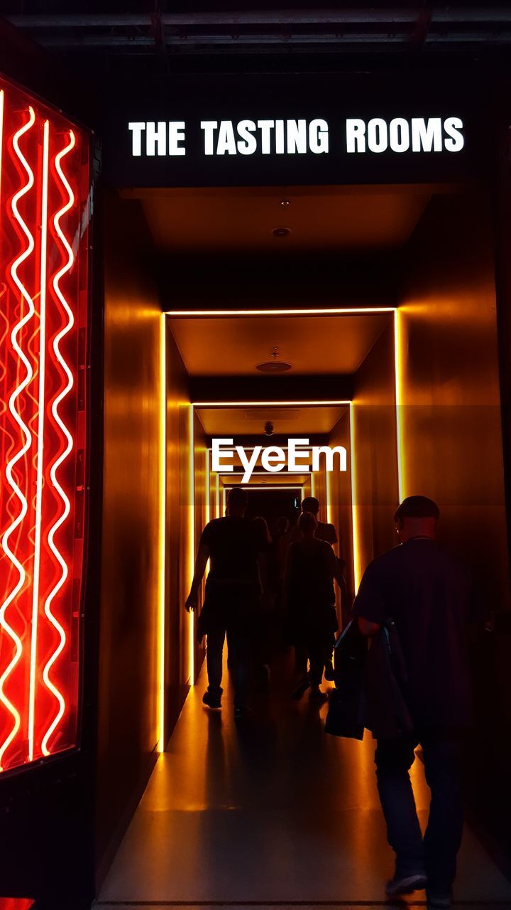 REAR VIEW OF PEOPLE WALKING IN ILLUMINATED UNDERGROUND ROOM