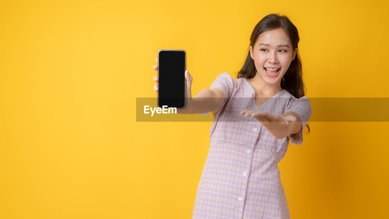 PORTRAIT OF SMILING YOUNG WOMAN AGAINST YELLOW BACKGROUND