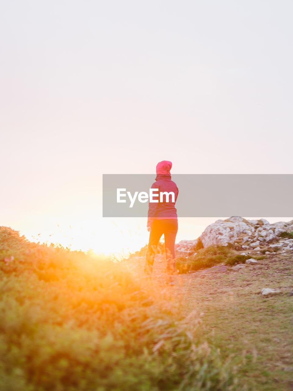 Rear view of woman standing on field against sky during sunset