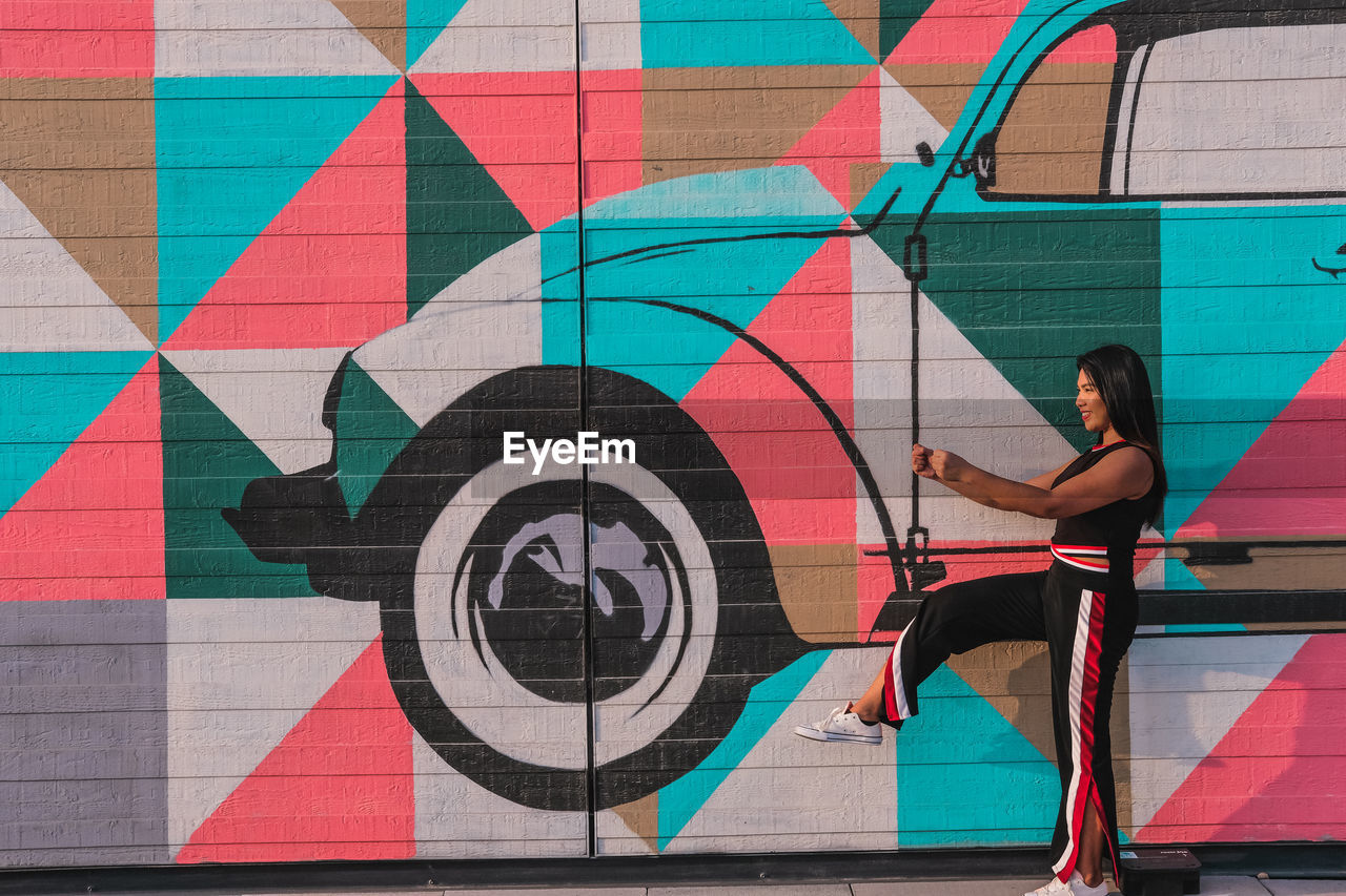 WOMAN STANDING ON MULTI COLORED WALL