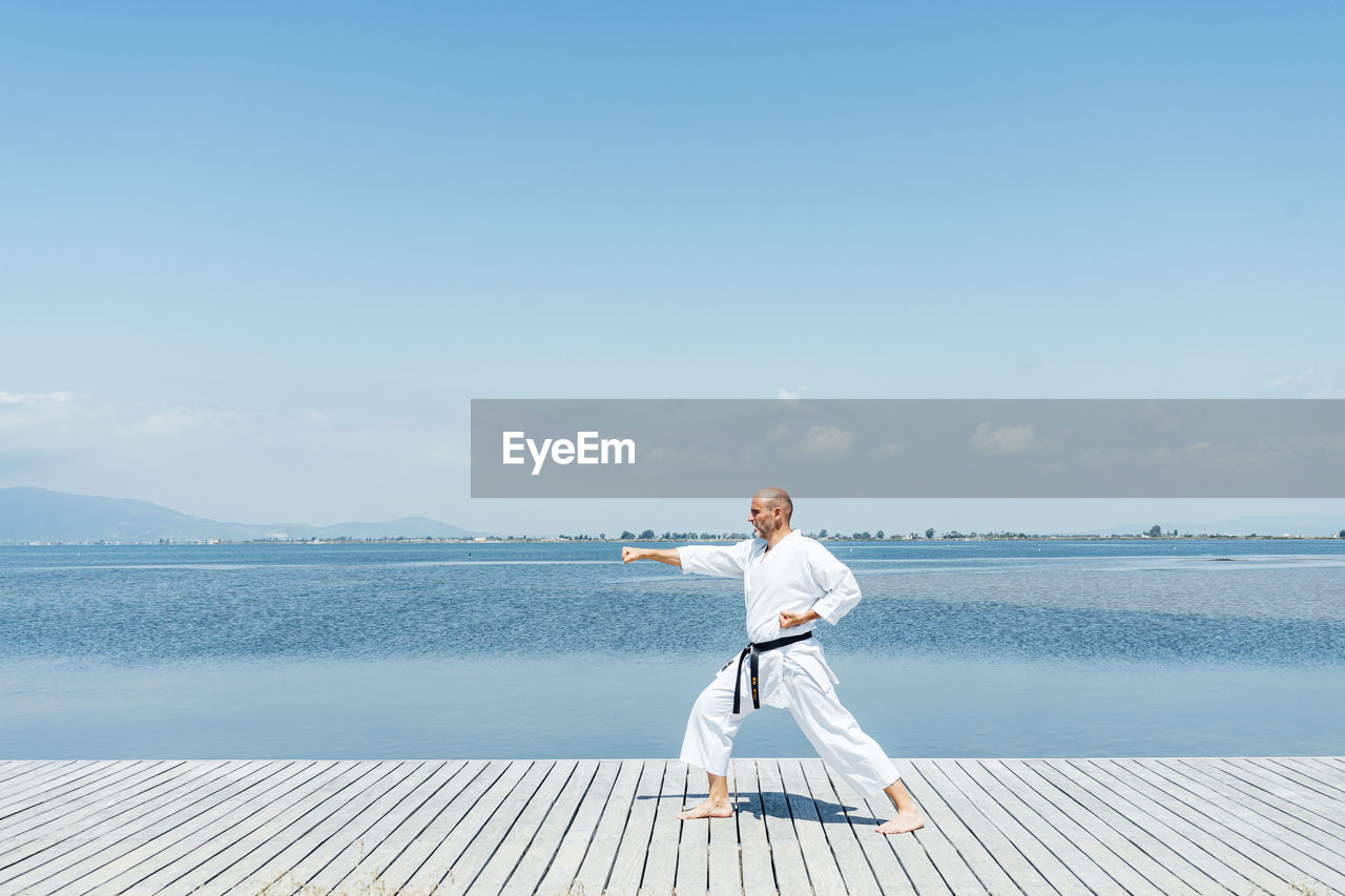 A man practices martial arts on a wooden walkway near the water