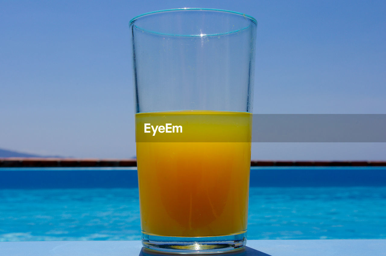 Close-up of orange juice on table against sea