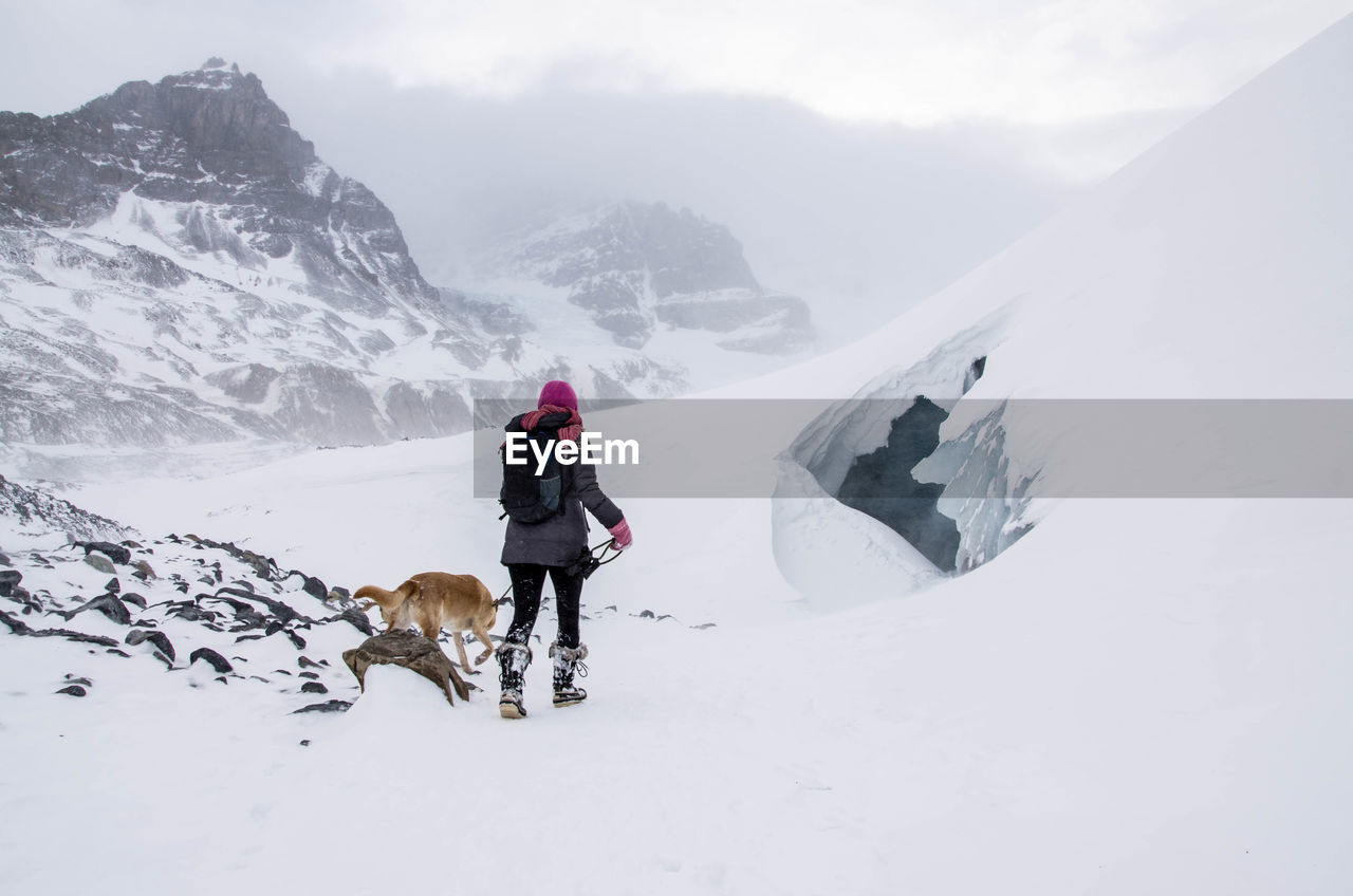 Woman with dog walking on snow covered mountains