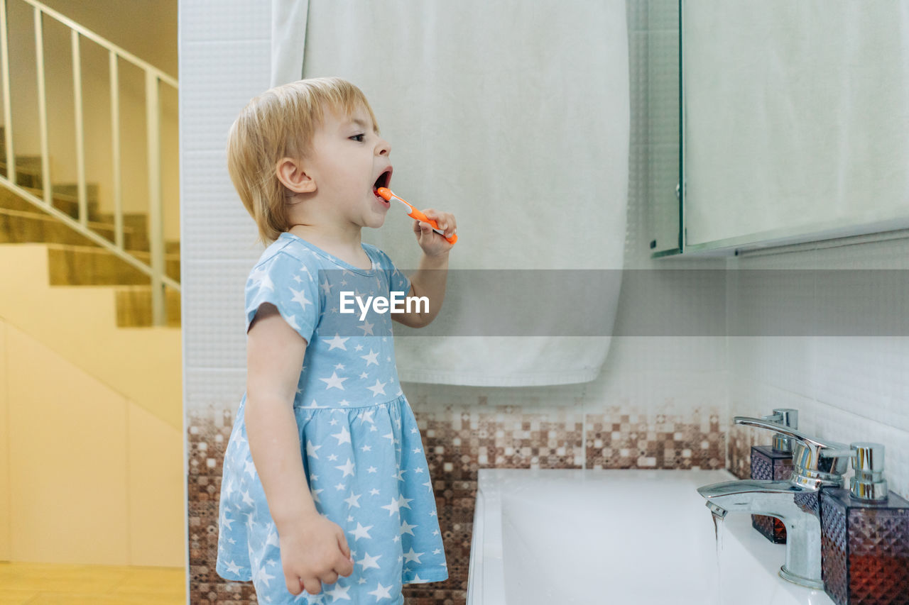 A little girl learns to brush her teeth on her own in the bathroom.