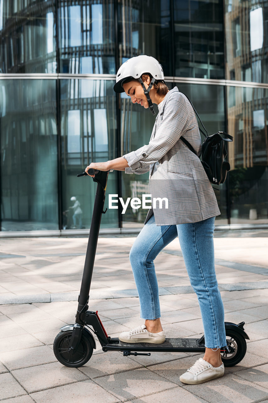 Young caucasian woman wearing cycling helmet standing outdoors with electric push scooter
