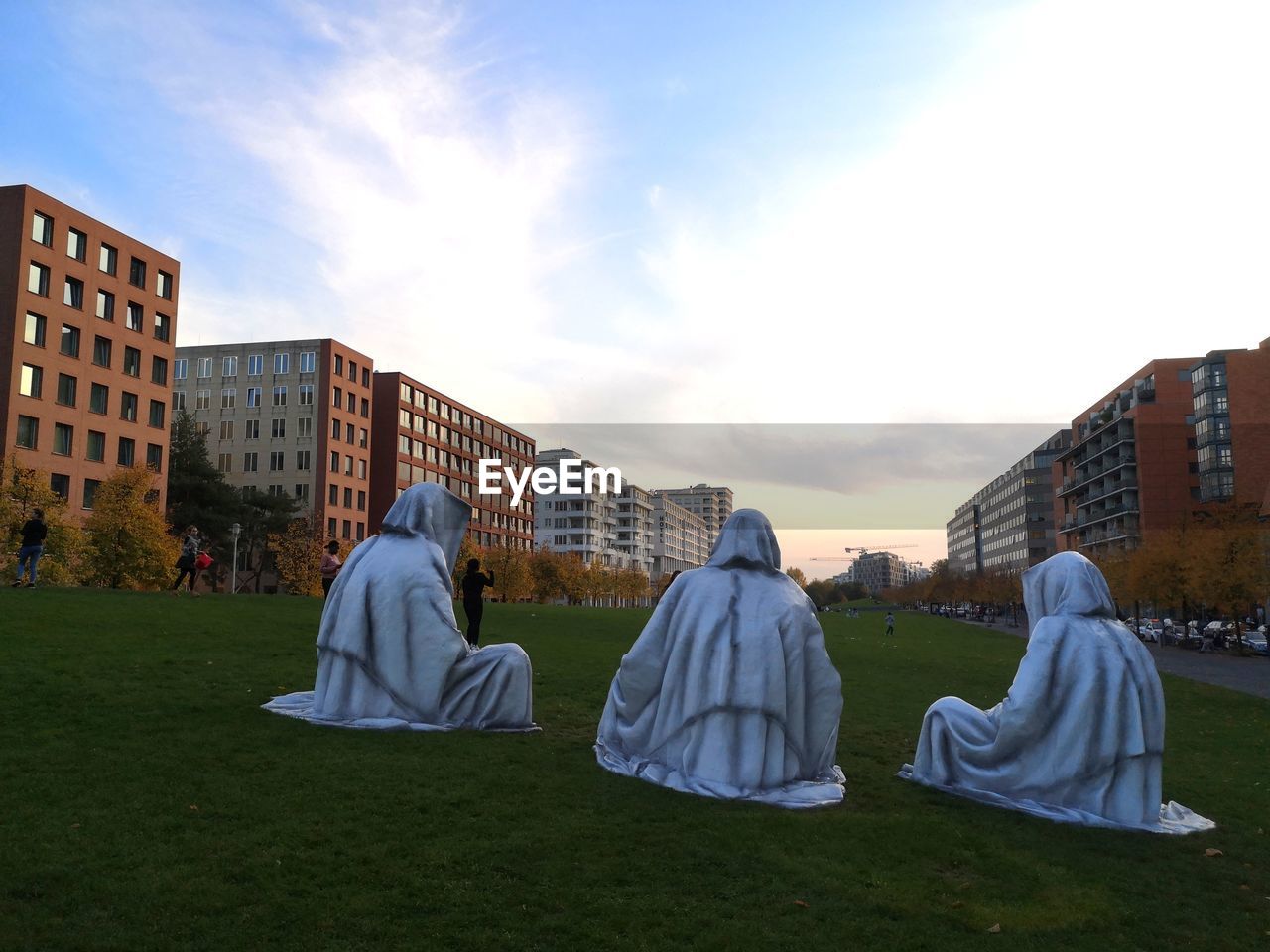 REAR VIEW OF PEOPLE ON FIELD AGAINST BUILDINGS