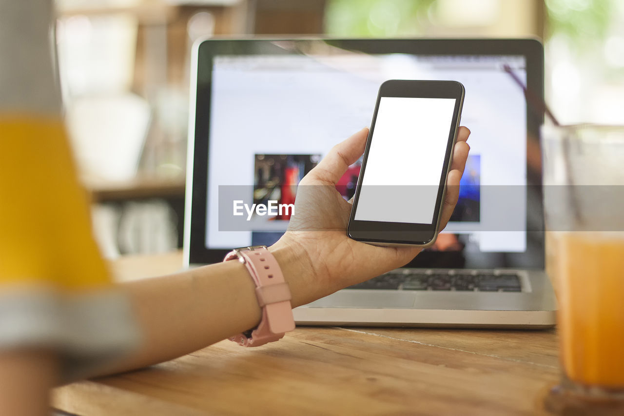 Cropped hand of woman using mobile phone at wooden table in office