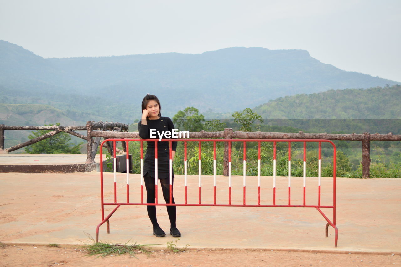 Full length portrait of woman standing by railing against mountains