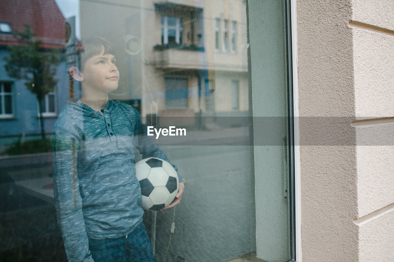 Boy with soccer ball standing by window