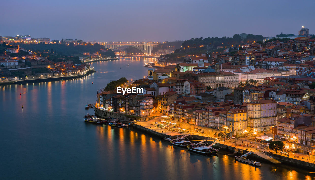 Buildings by river in city at dusk