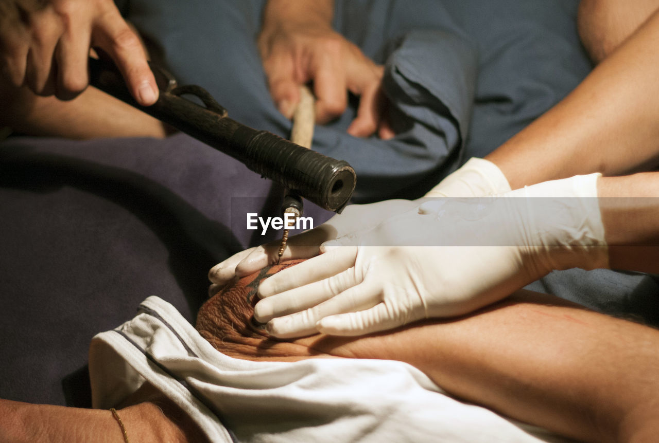 Cropped hands of people making tattoo on man shoulder with tools