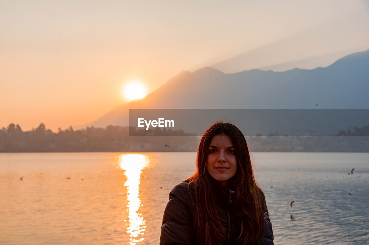 Portrait of young woman against lake during sunset