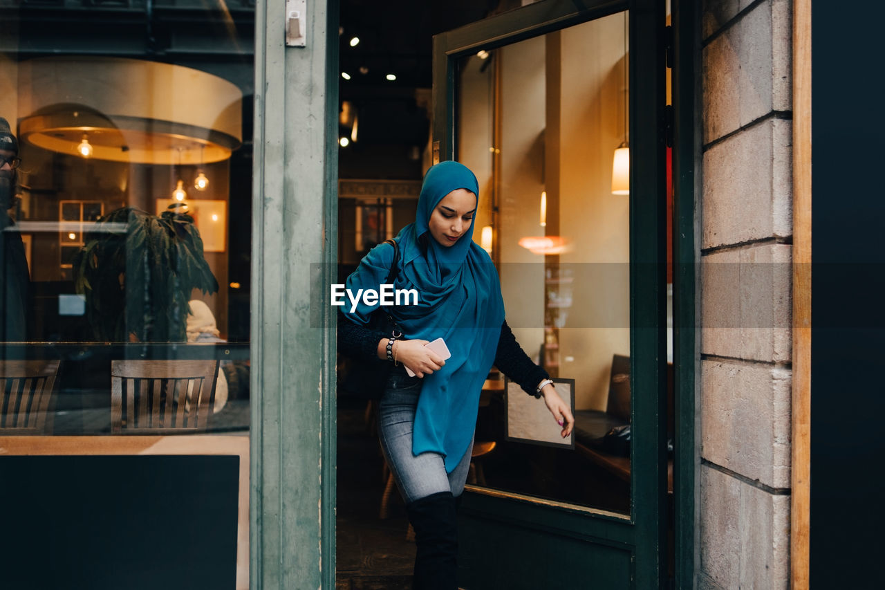 Young woman wearing hijab leaving store in city