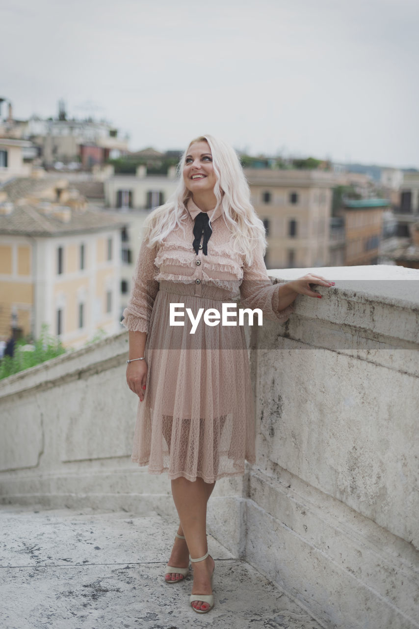 FULL LENGTH OF WOMAN STANDING AGAINST BUILDING