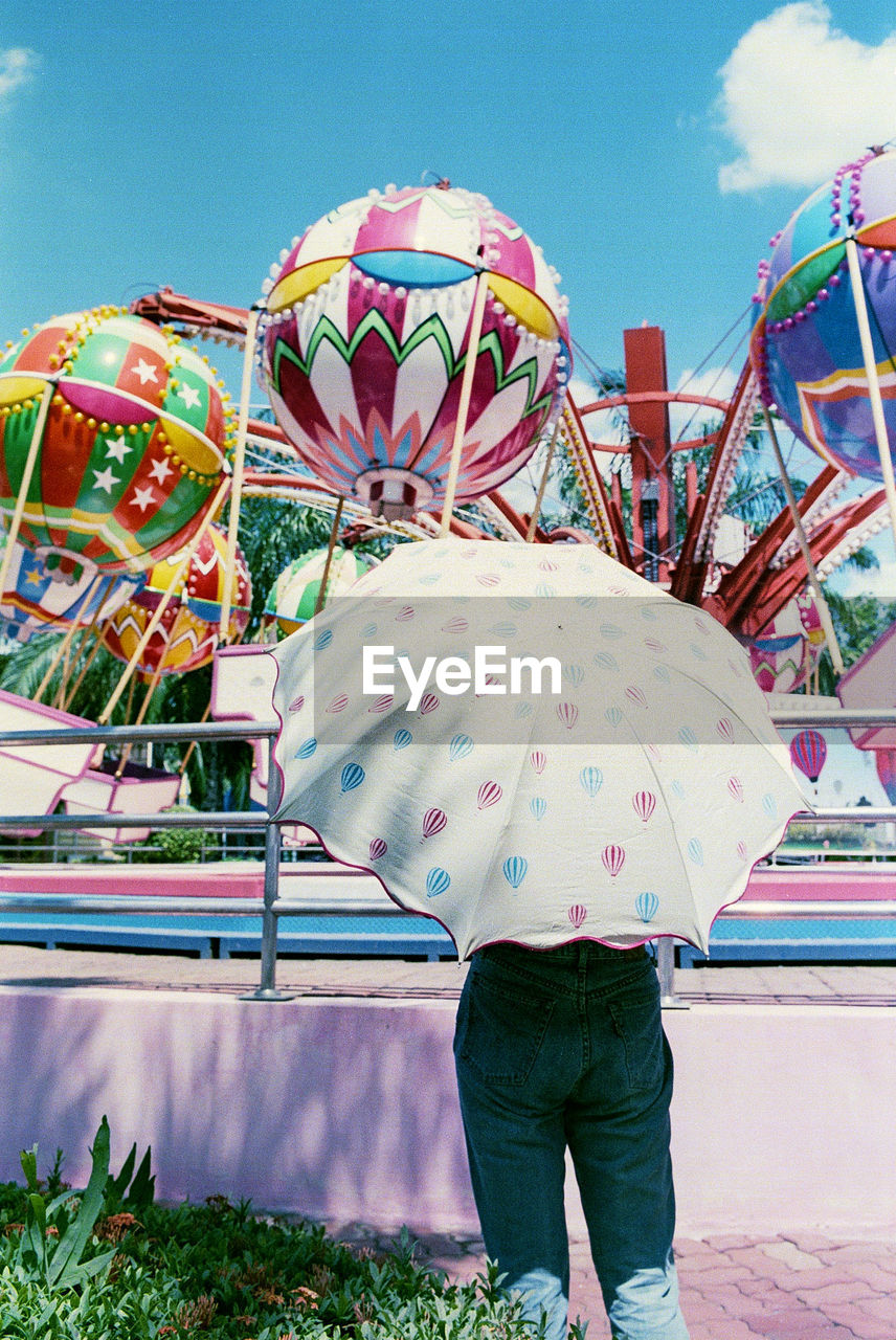 Rear view of person standing under umbrella at amusement park