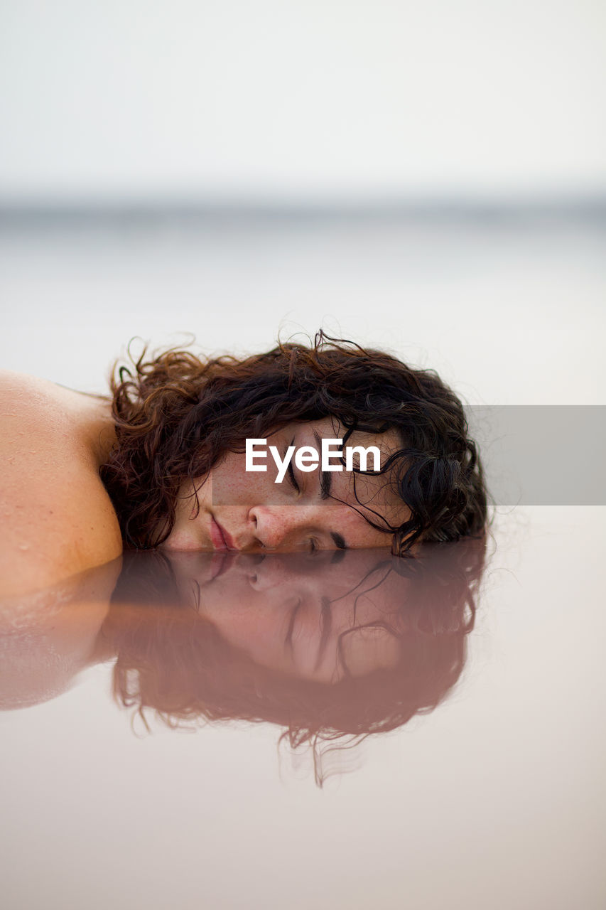 Tranquil female with closed eyes lying with half of face in water of pink pond in summer