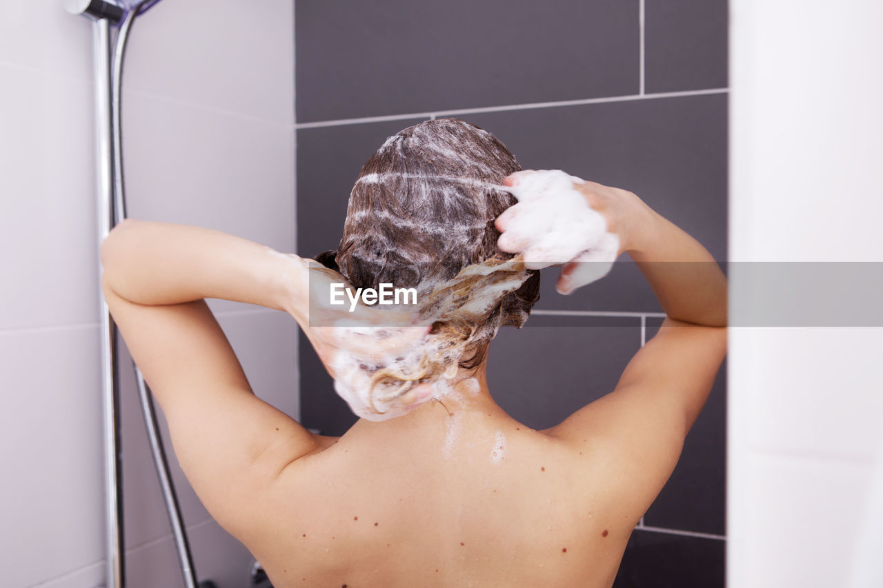 Rear view of shirtless woman washing hair while bathing in bathroom