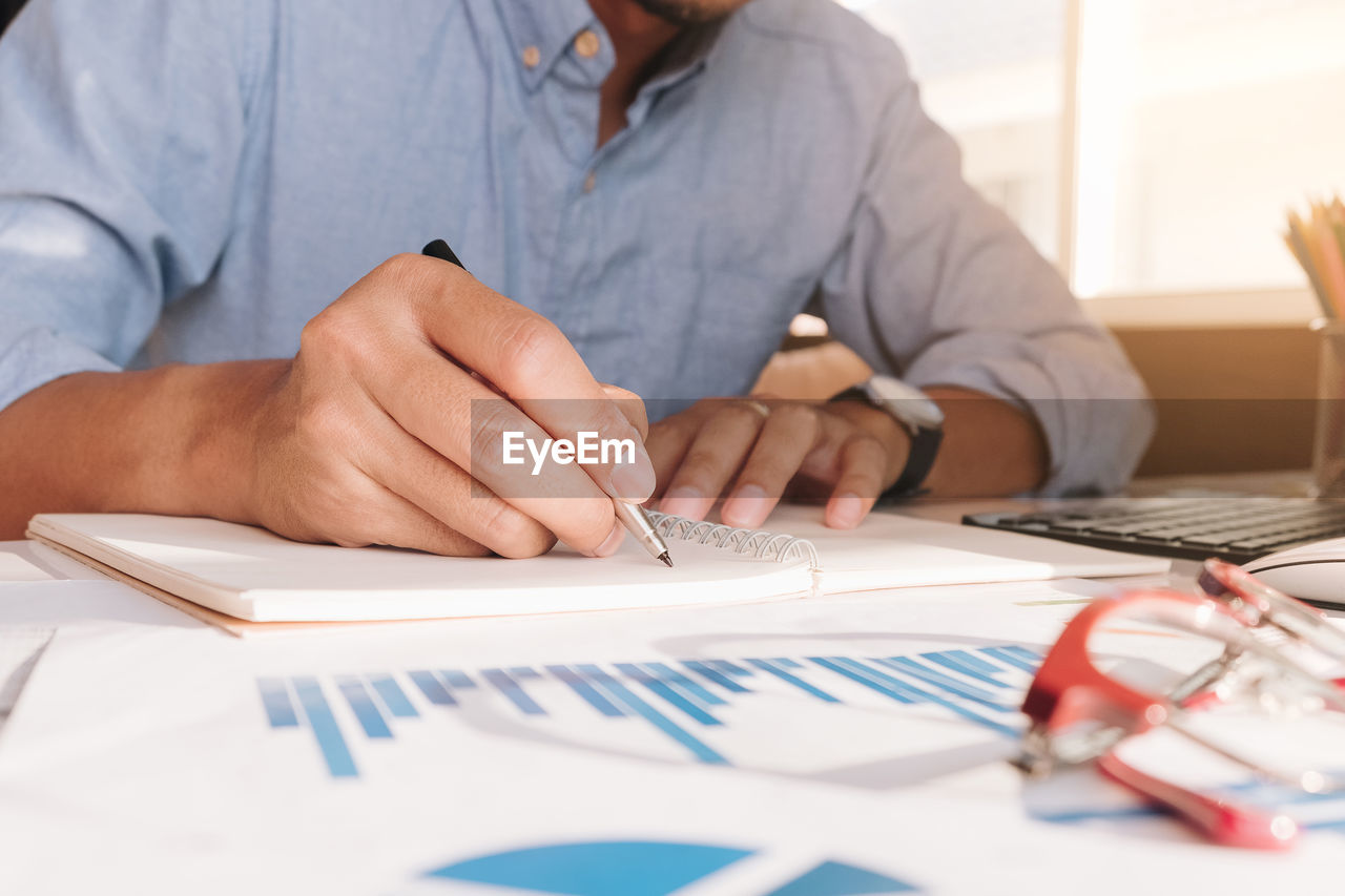 MIDSECTION OF WOMAN WORKING ON PAPER WITH TABLE