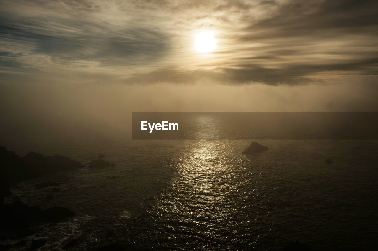 Scenic view of sea against sun shining in cloudy sky