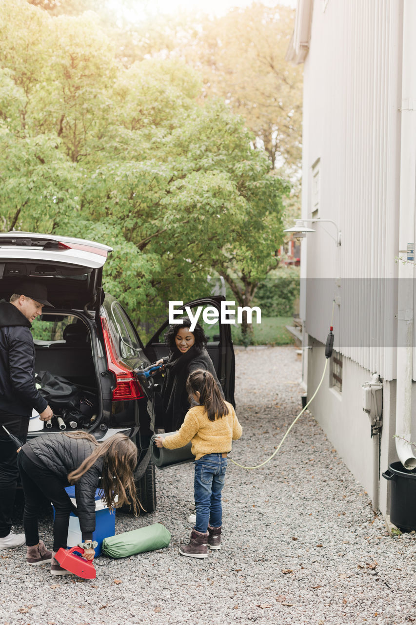 Family loading luggage in electric car while going for picnic