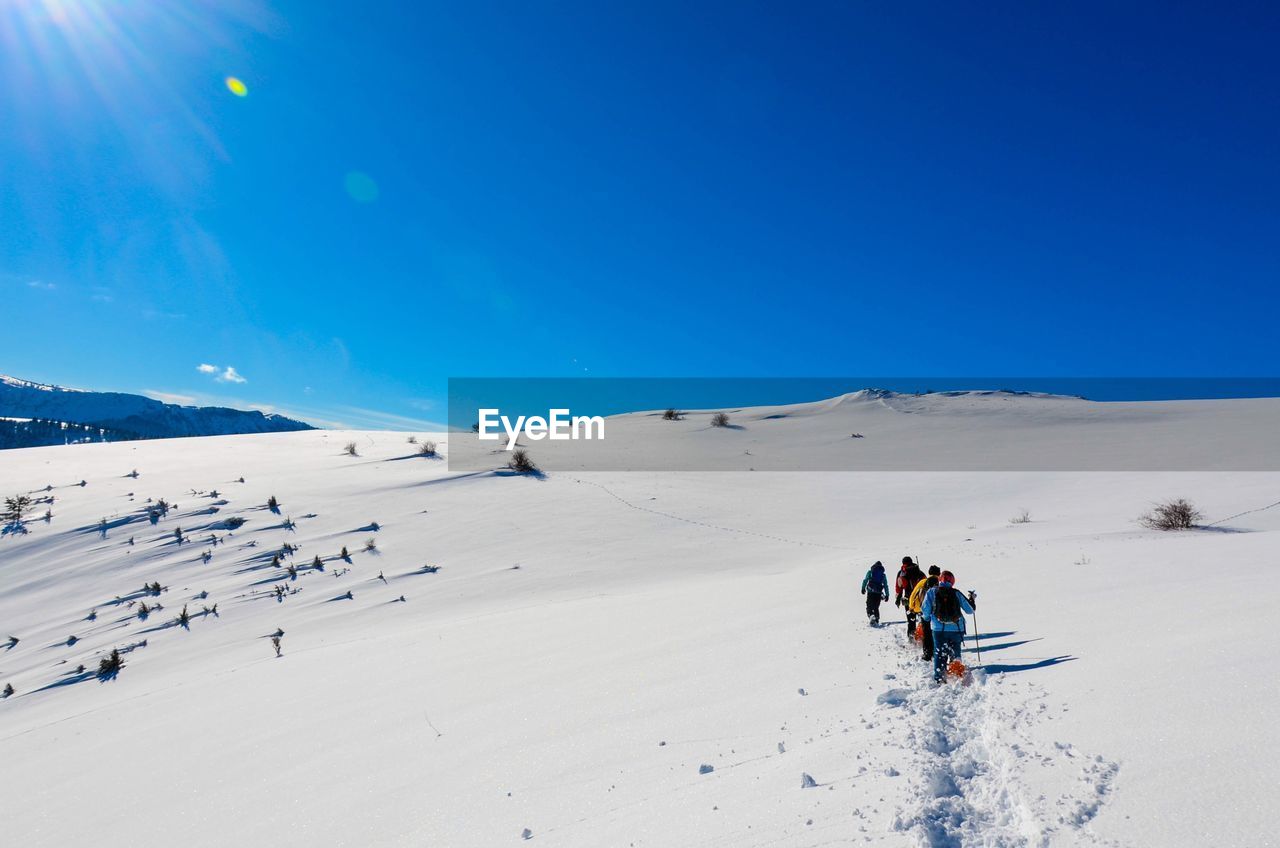 People hiking on snowy landscape against clear sky