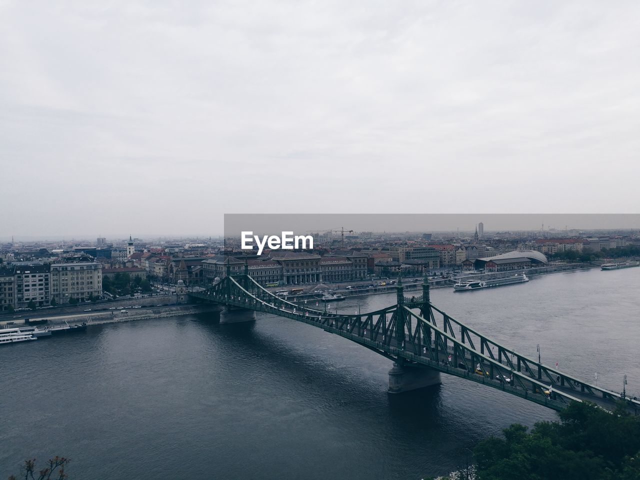 Bridge over river in city against cloudy sky