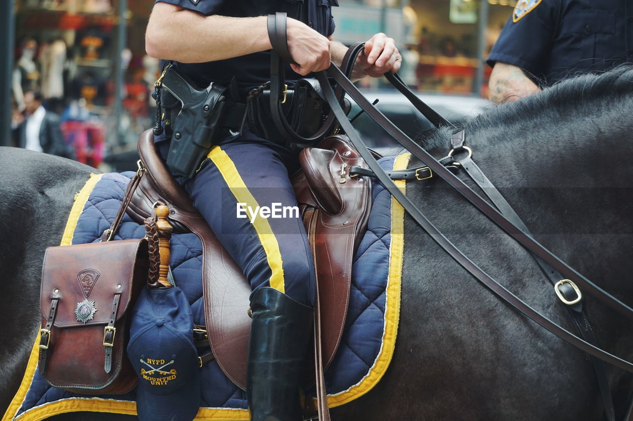 Midsection of police officer riding horse in city