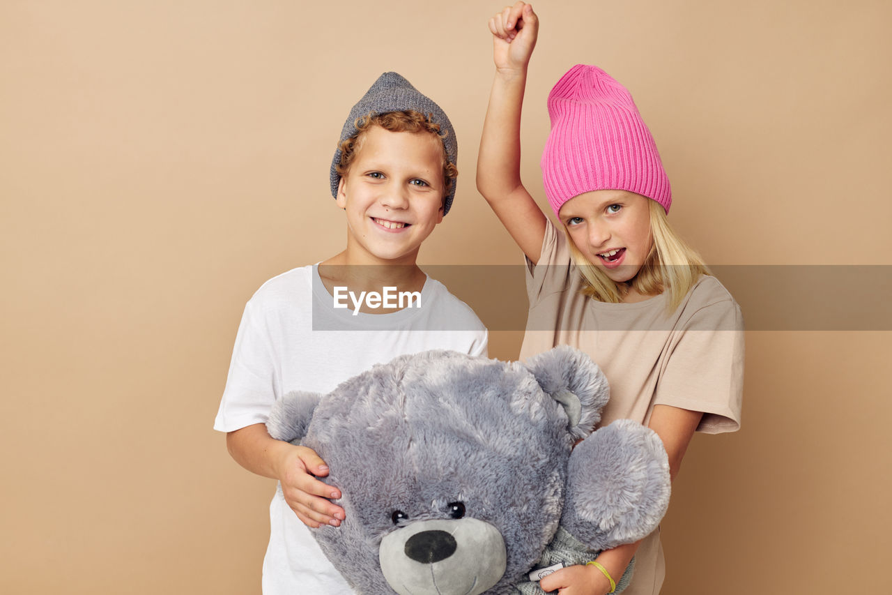 Portrait of sibling holding stuffed toy against beige background