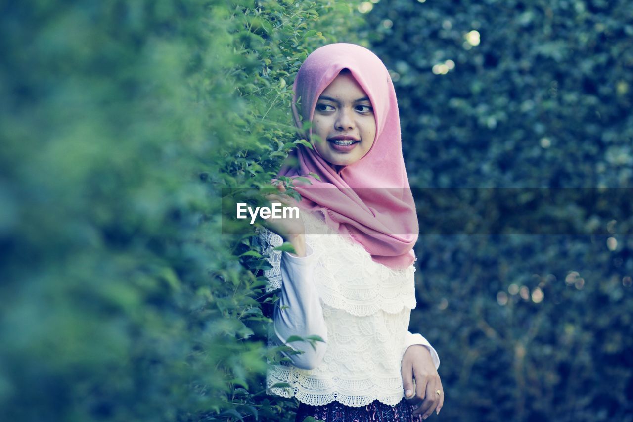 Side view of thoughtful young woman wearing hijab while standing by plants