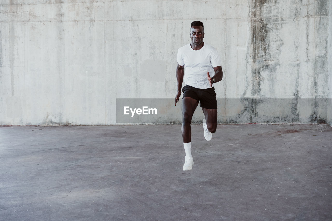 Serious male athlete jumping against white wall