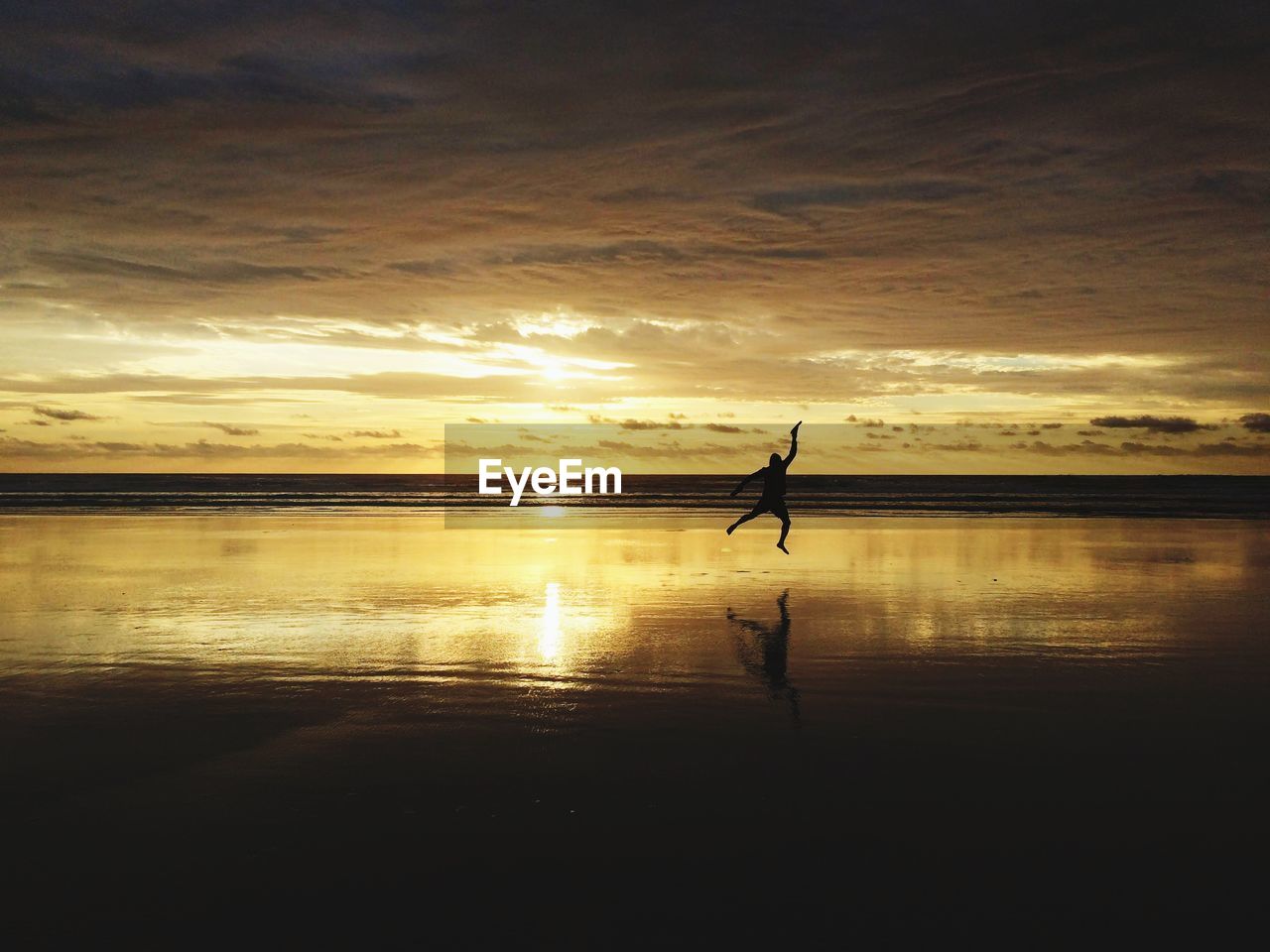 Silhouette of man jumping at beach against sky during sunset