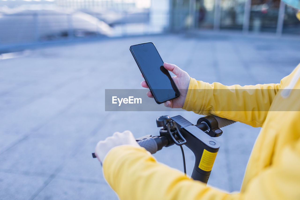 Young woman in yellow coat prepares and uses her electric skateboard.