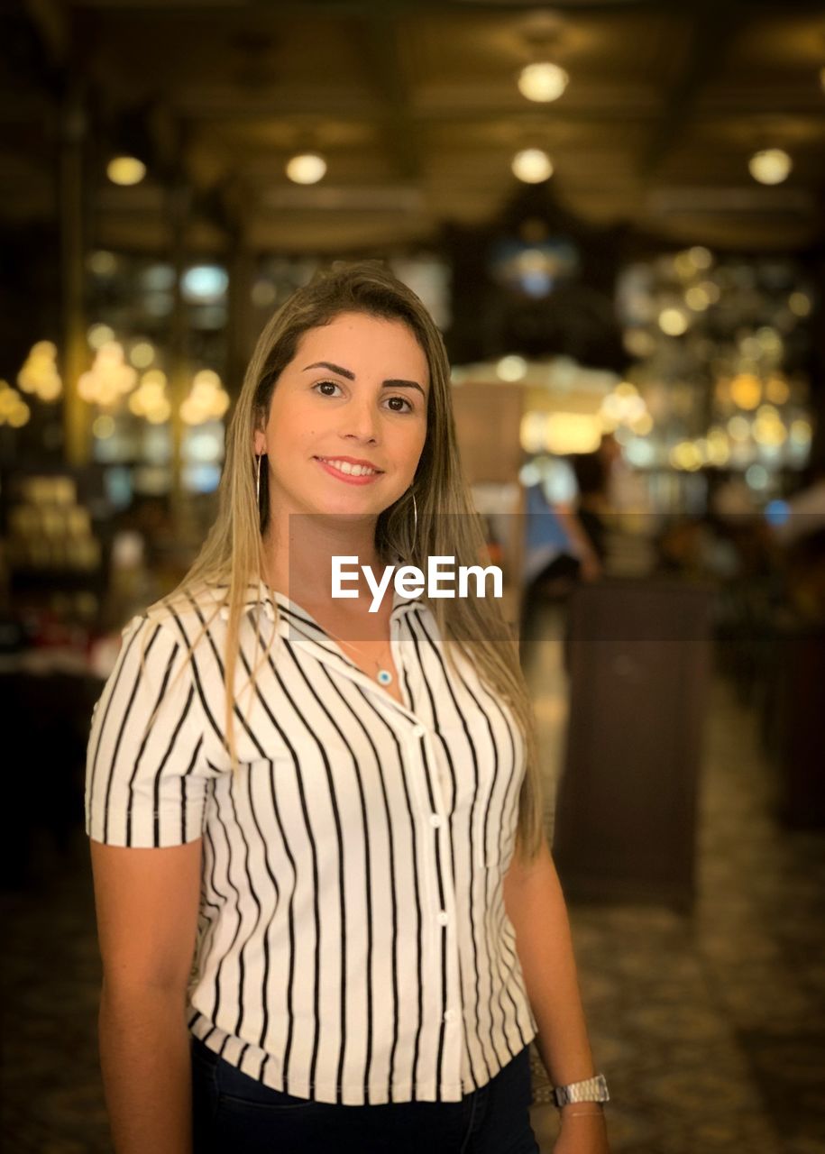 Portrait of smiling young woman standing in bar