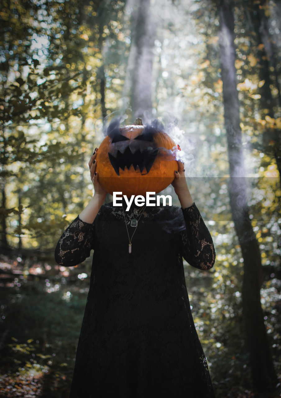 Woman wearing jack o lantern standing in forest