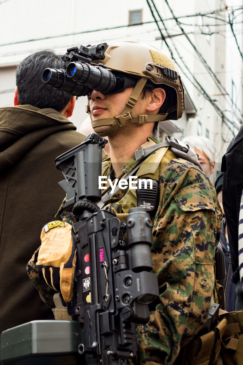 PORTRAIT OF MAN HOLDING CAMERA WHILE STANDING AGAINST