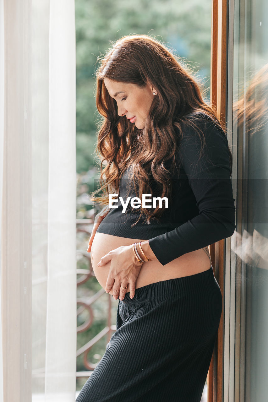 young woman looking through window at home