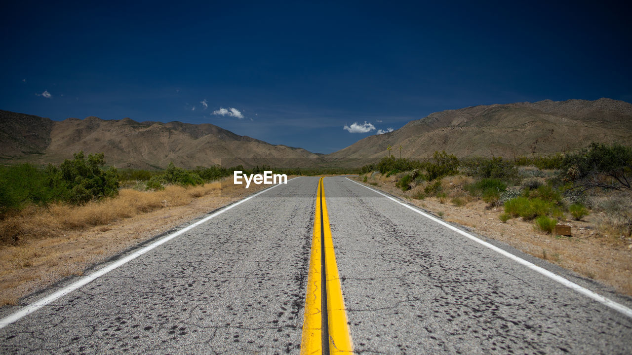 Road leading towards mountains against blue sky